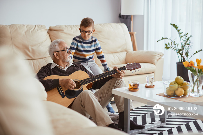 Senior man plays acoustic guitar to his grandson at home.