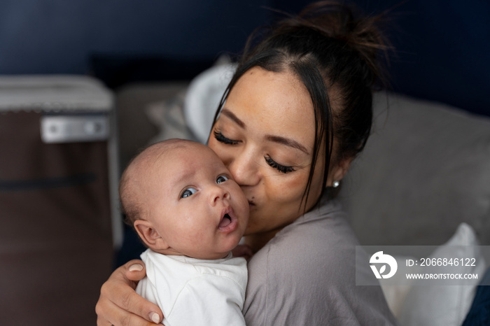 Portrait of mother kissing newborn baby girl at home