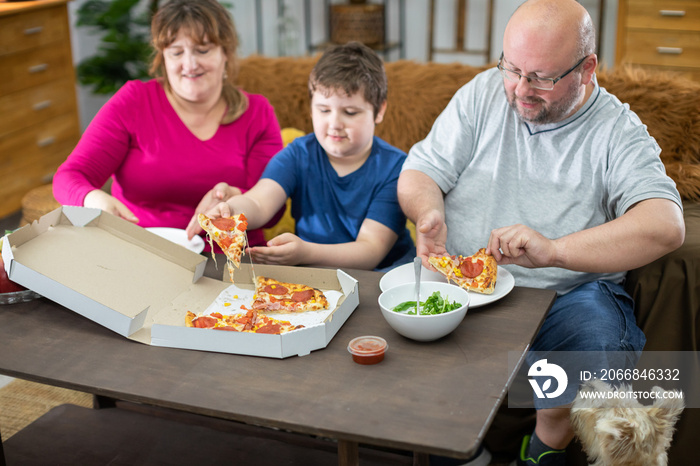 The family distributes slices of pizza to the whole family and the dog waits his turn.