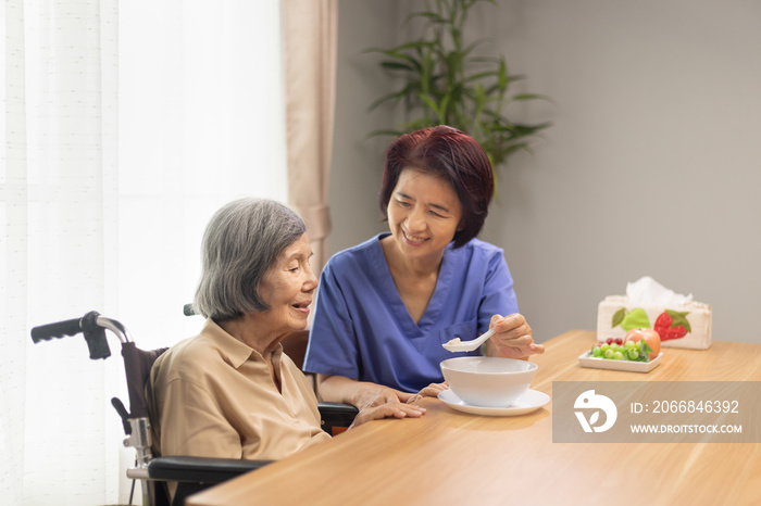 Caregiver feeding elderly asian woman with soup.