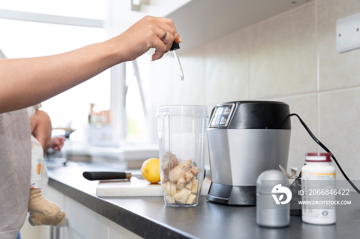 Mother preparing smoothie with vitamins while carrying baby girl in kitchen