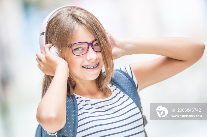 Happy smiling schoolgirl with dental braces and glasses listening music from headphones..  Orthodontist and dentist concept