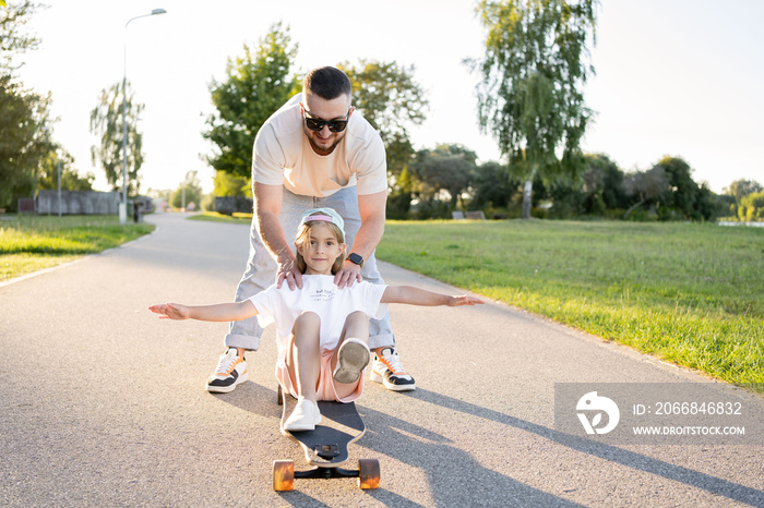 Playful young man and preschooler girl enjoying having fun time together at summer. Family activities concept. Child riding sitting on skateboards outdoor.