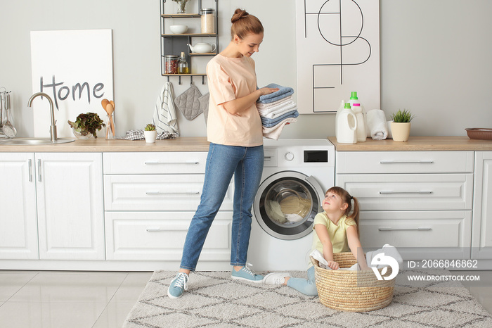 Woman and her cute little daughter doing laundry at home