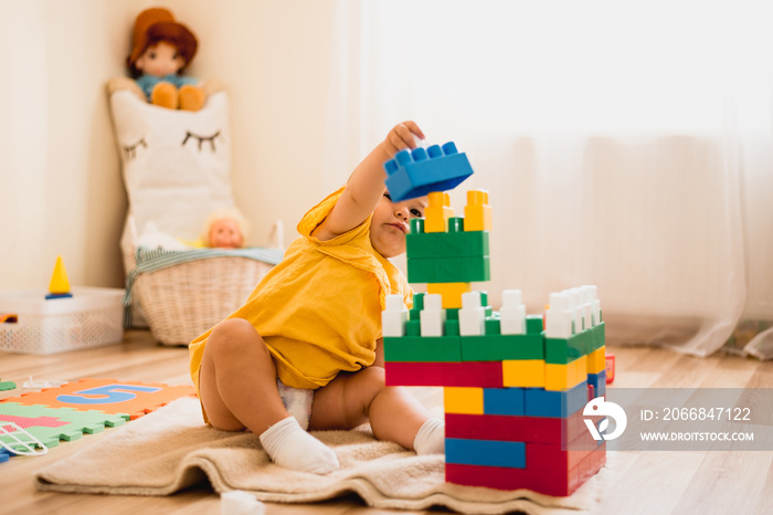 little girl playing with construction toy blocks building a tower in a sunny kindergarten room