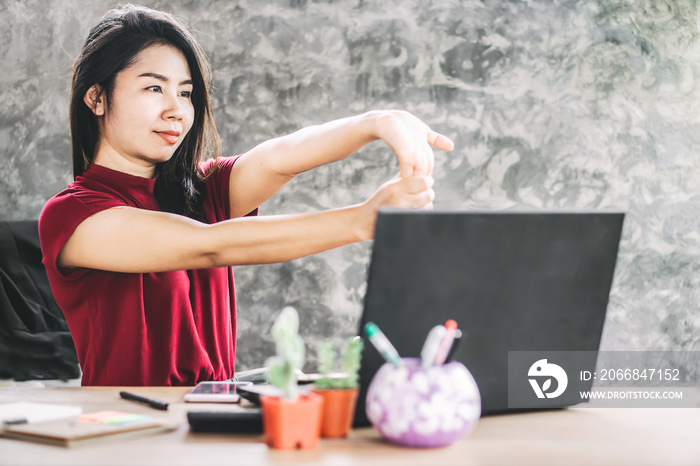 Asian business woman stretching arm, hand and finger to relaxing muscle and body at office desk