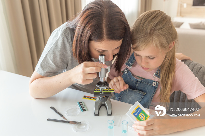 Mother and young daughter doing some experiments with microscope at home