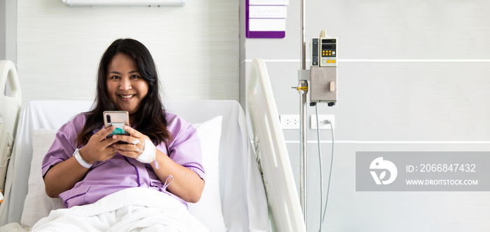 Asian fat woman patient using smartphone on bed in the new medical center. Recovery Room with beds and comfortable medical