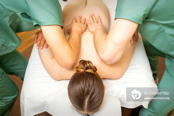 Back and hands double massage with four hands of two professional massagers for a young caucasian woman in a spa salon