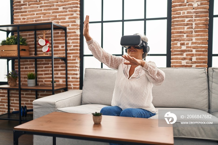 Middle age woman playing video game using virtual reality glasses at home