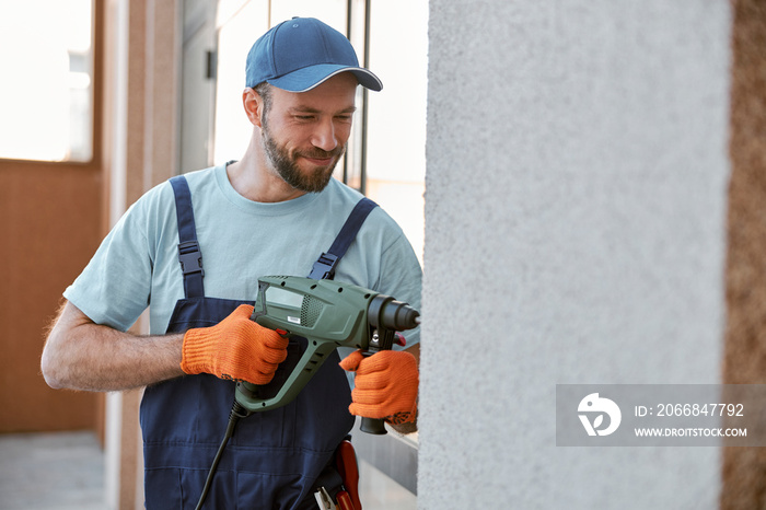 Bearded young man drilling wall with hammer drill