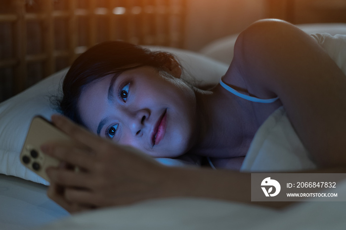 Beautiful young Asian woman is using smartphone to text while getting ready for bed