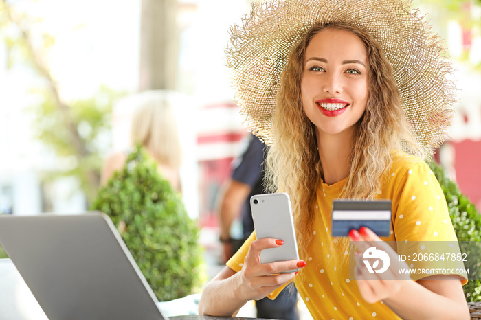 Young woman with credit card, mobile phone and laptop sitting in cafe