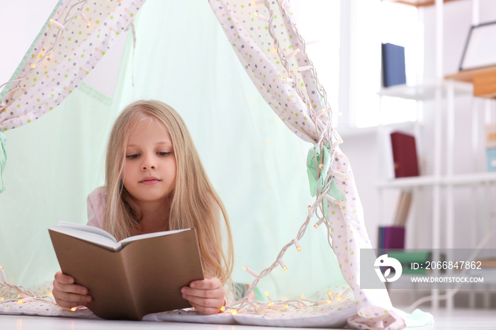 Cute little girl reading book in hovel at home