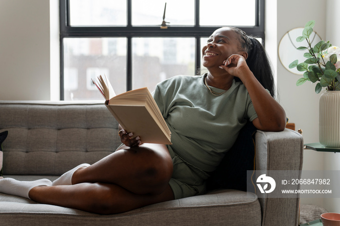 Young woman reading book while resting on sofa at home