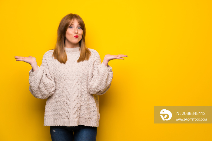 Redhead woman over yellow wall having doubts while raising hands