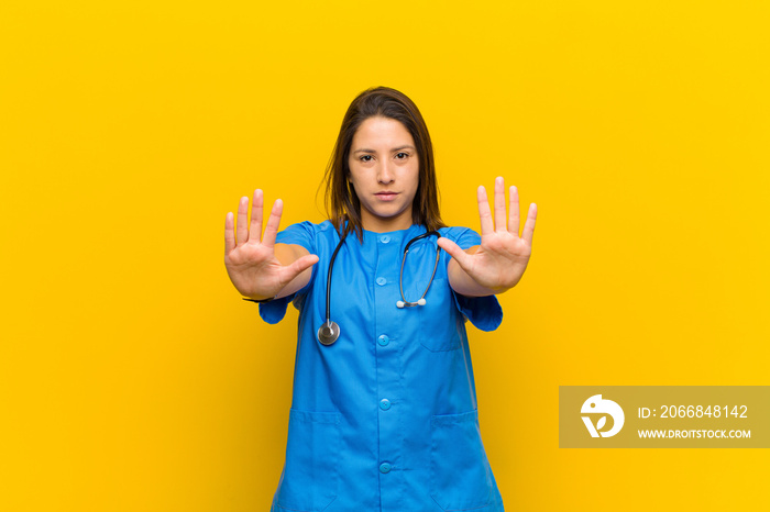 looking serious, unhappy, angry and displeased forbidding entry or saying stop with both open palms isolated against yellow wall