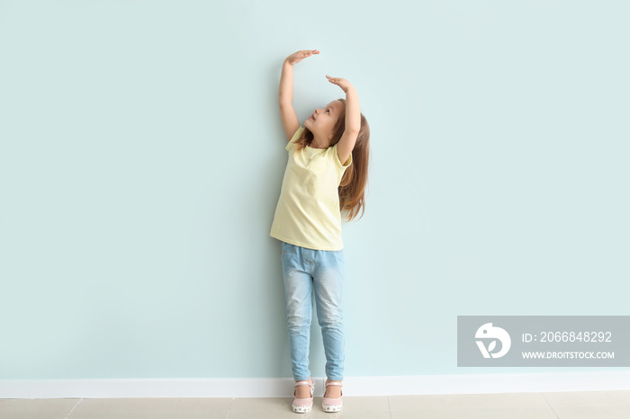 Cute little girl measuring her height near wall