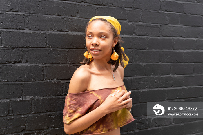 Portrait of young woman looking away while standing against brick wall