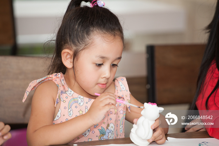 Cute little girl student painting a ceramic pottery model  in classroom school . kid artist . child sitting at desk preschool . Early education . Children in kindergarten.