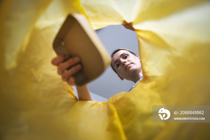 paper waste sorting and recycling - woman throwing piece of cardboard in yellow bag