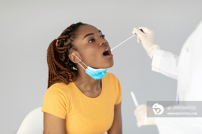 Doctor making oral covid PCR test for young black female patient over grey studio background