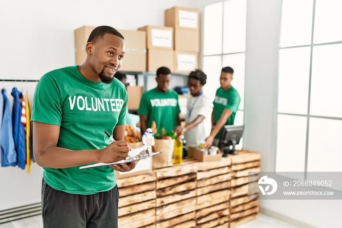 Group of young african american volunteers working at charity center. Man smiling happy writing on clipboard.