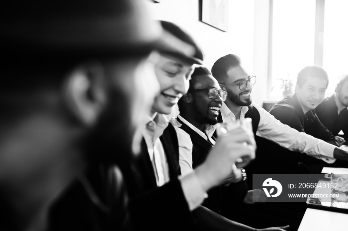 Group of handsome retro well-dressed man gangsters spend time at club, sitting and drinking whiskey. Multiethnic male bachelor mafia party in restaurant.