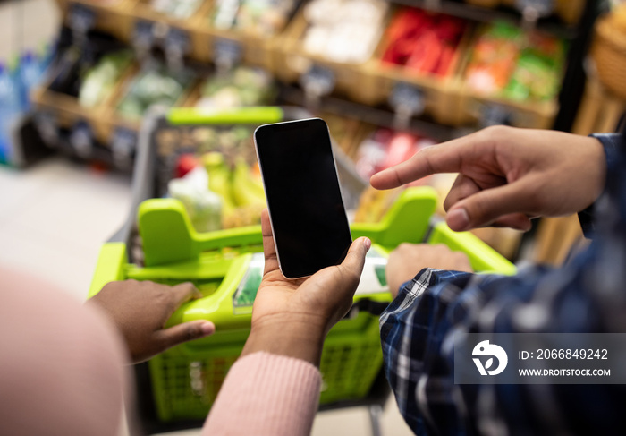 Unrecognizable black couple holding smartphone with empty screen at supermarket, mockup for your mobile app or website