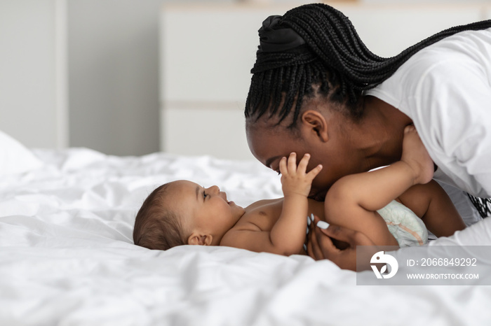 Black mom playing with her infant, kissing baby in belly