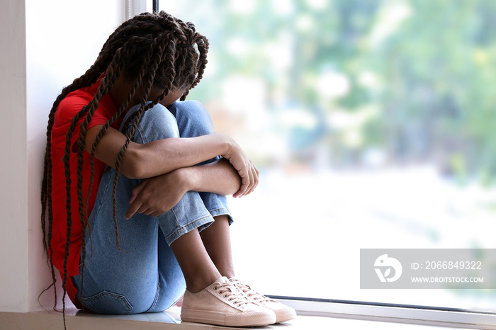 Sad African-American girl sitting on windowsill. Stop racism