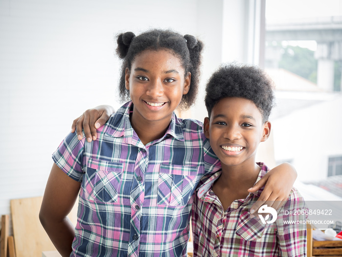 Two African American brothers and sisters hug the neck and look camera’s smile. Older sister hugs little brother by the neck.