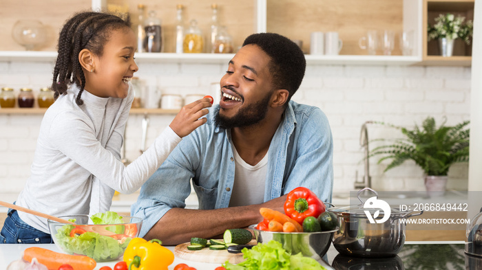 Lovely afro girl giving her dad tomato to taste