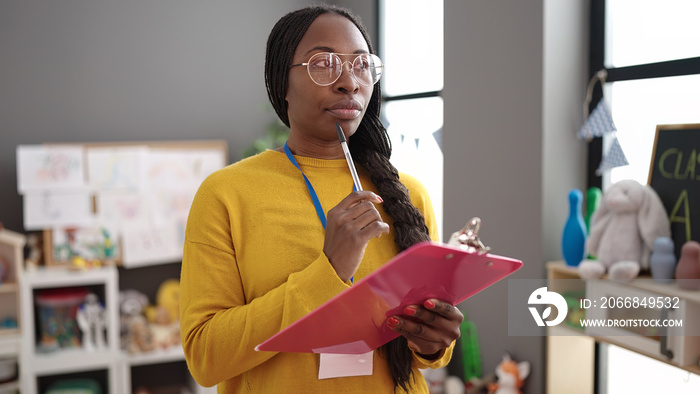 African woman working as teacher writing on clipboard at kindergarten