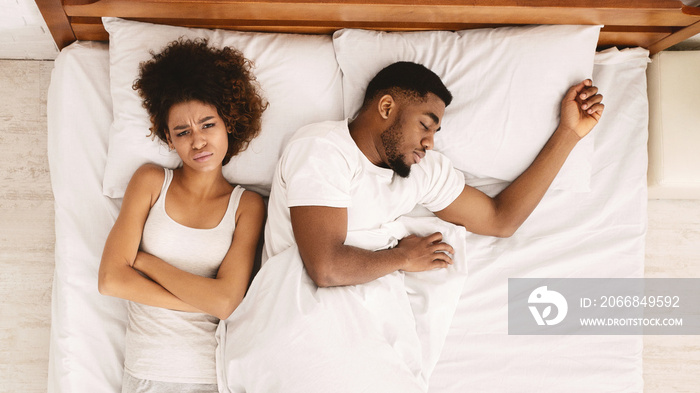 Sad woman lying in bed with sleeping man