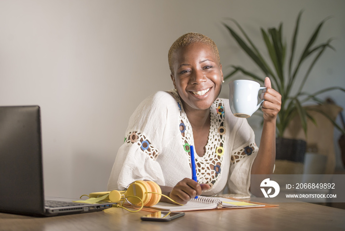 young happy and attractive hipster black afro American woman drinking tea or coffee at home office working cheerful with laptop compute