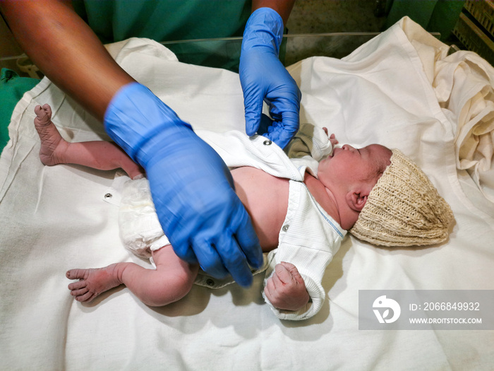 Midwife and surgeon with clinical protective gear are inspecting and cleaning newborn baby after caesarean section. Child and birth concept.