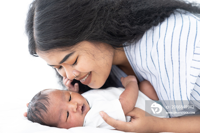 African American mum hugging and kissing her newborn baby on white bed. Close up of infant with young mother