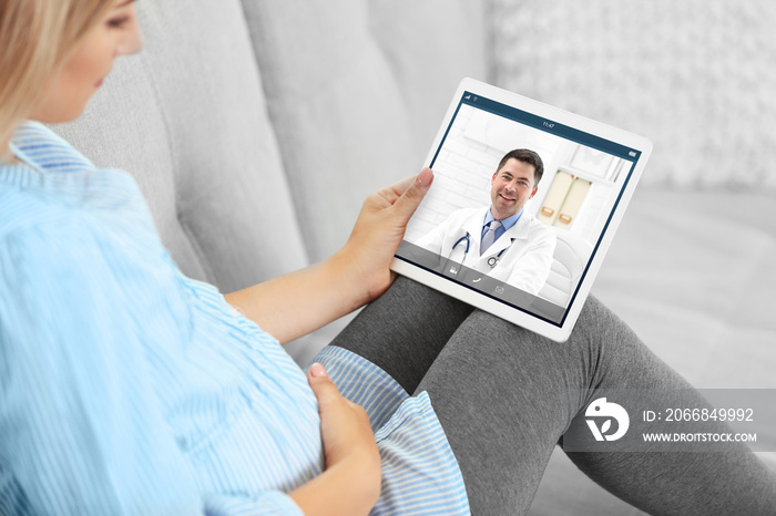 Pregnant woman video chatting with doctor on tablet. Professional medical online consultation concept.