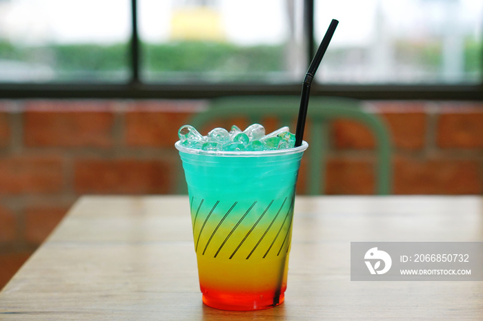 Colorful Cocktail or Tropical Mocktail - Plastic glass of Energy Drink with lemonade, orange juice and watermelon syrup on wooden table and on blurred background.