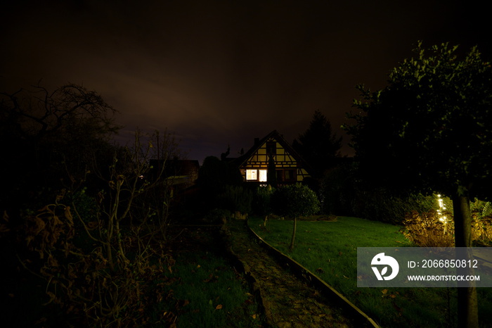 dark half-timbered house with dark mystical illuminated decorated green garden under the stars in an autumn night