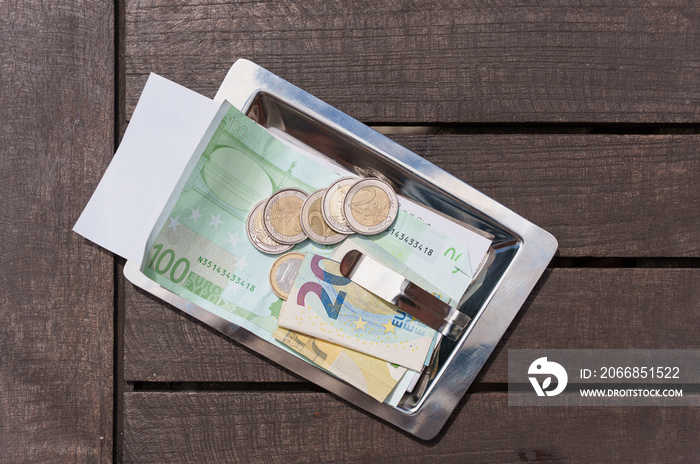 Restaurant customer leaves tips to the waiter, generous tips with cash and coins in the check tray. Cash payment for privacy and anonymity in the world of banking and credit cards.