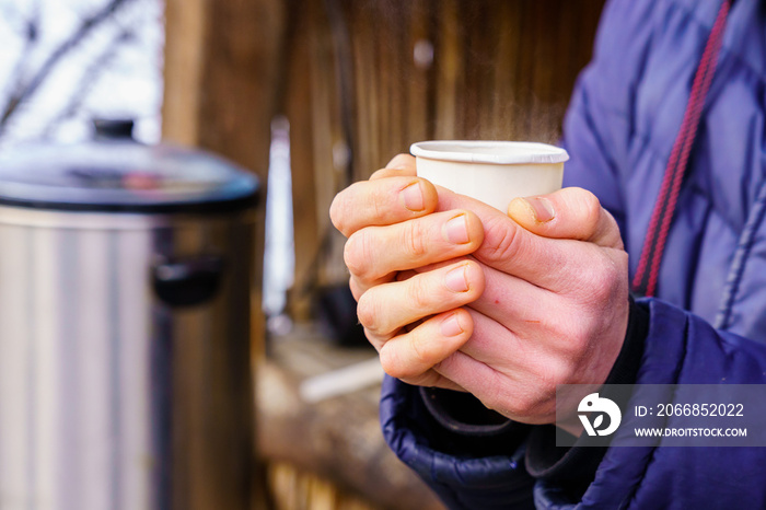 Frozen hands hold a disposable paper cup with hot tea. Warming in cold winter. Selective focus. Background