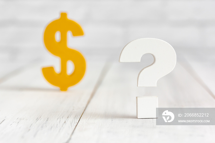 Question mark with dollar sign on white wood table over white brick background with copy space.