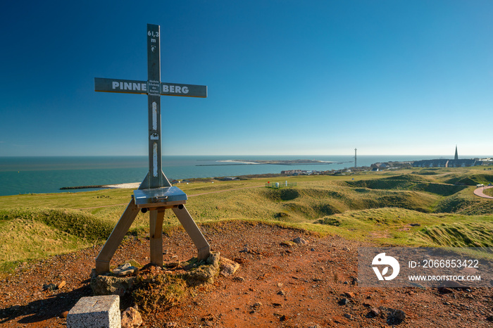 Iron cross on top of Pinneberg, the highest point of the island of Helgoland. Beautiful sunny day of winter in German archipelago with Northern sea and Dune island in the back.