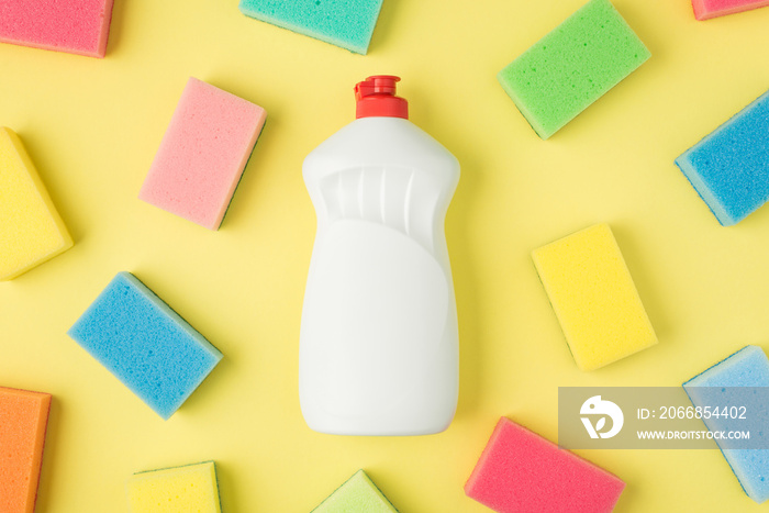 Top view photo of detergent white bottle without label and multicolor sponges on isolated yellow background with copyspace