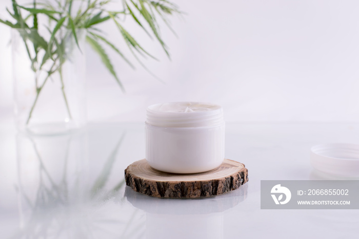 Natural cosmetics with cannabis oil. Mockup with a White clean jar with cosmetics cream and green leaves of hemp.