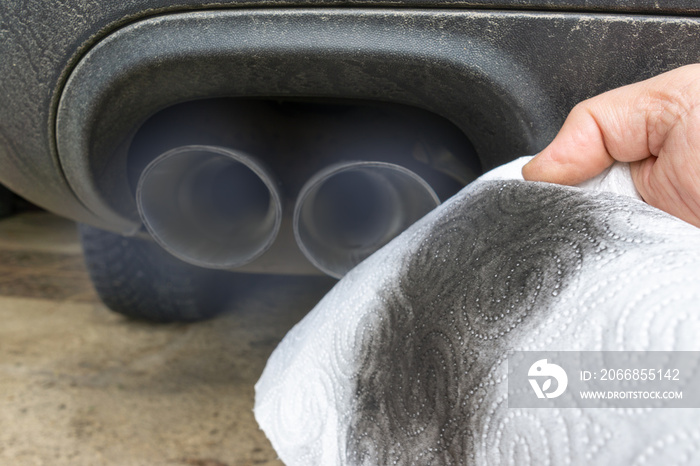 Hand holding a dirty white cloth in front of the smoking exhaust of a car with diesel engine.