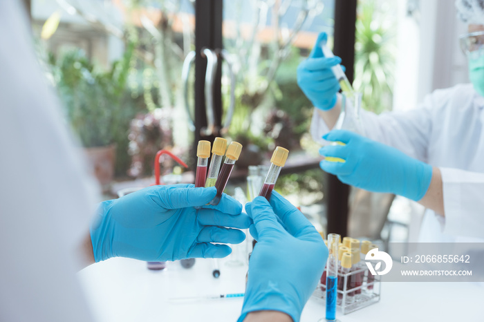 Microbiologist or scientist doctor wearing biohazard protection clothing with a tube of biological sample contaminated coronavirus Covid 19 infected blood sample.