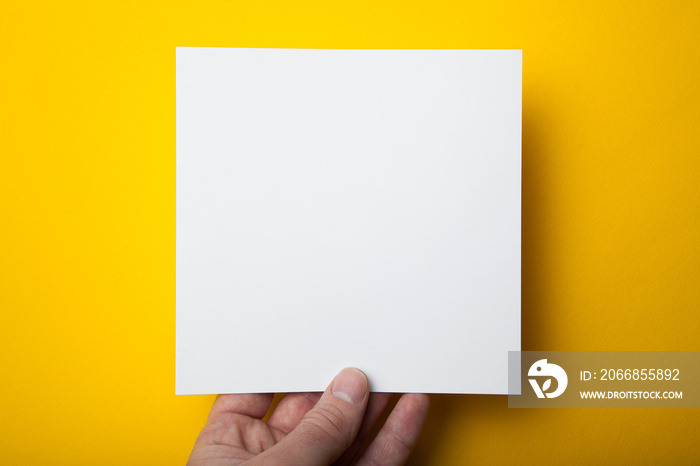 A square layout of a white paper in a hand on a yellow background.